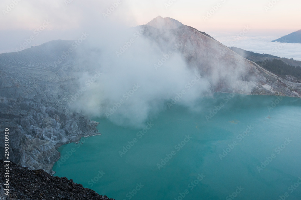 Crater of a volcano with a green sulfuric volcanic lake and volcanic smoke. View of the smoking volcano Kawah Ijen in Indonesia. Mountain landscape