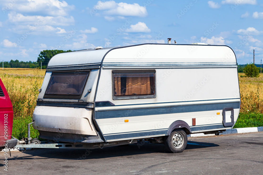 A motor home in the form of a white trailer in a parking lot near the road, secured to the car while traveling in remote uninhabited places. Movable property.