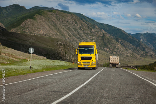 A large yellow truck rides on a highway in the mountains while transporting goods over long distances. Fast delivery by ground transportation.