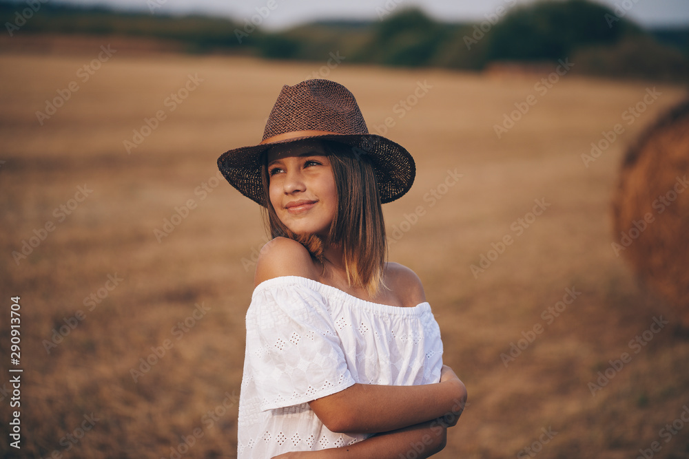 Obraz premium Little girl in a field with hay rolls at sunset