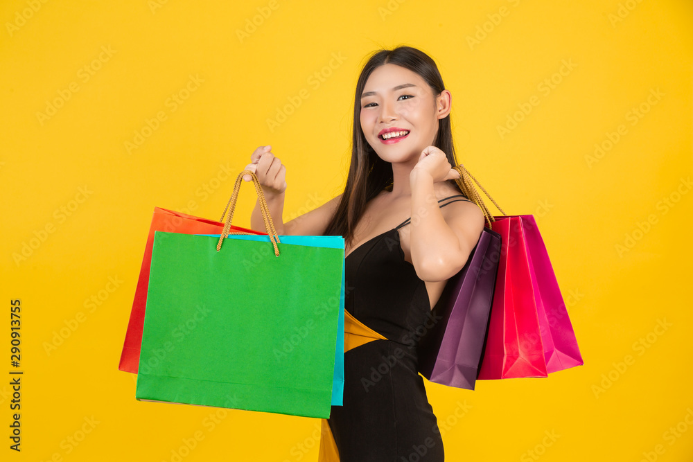 Shopping concept of a beautiful woman holding a colorful paper bag on a yellow background.