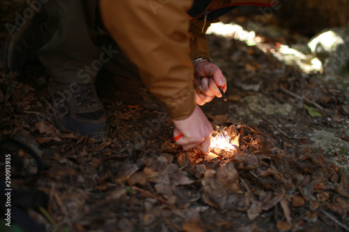 Close up view of campfire ignition by flintstone. Person in a brown windbreaker tries to make a fire with a flint sitting on fallen leaves in natural shelter.