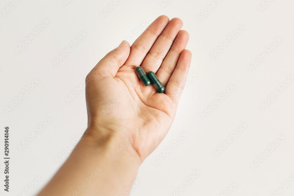 Dietary supplements. Hand holding spirulina capsules on white wall background. Morning vitamin nutrient pill. Health support and treatment. Biologically active additives