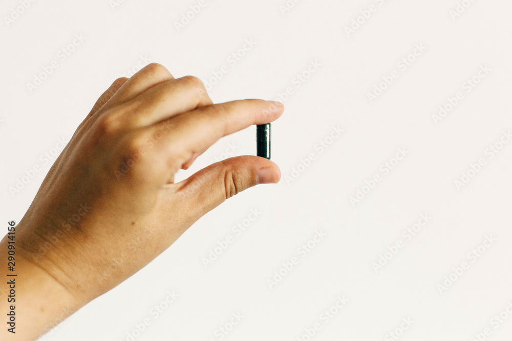 Dietary supplements. Hand holding spirulina capsule on white wall background. Morning vitamin nutrient pill. Health support and treatment. Biologically active additives Dietary supplements. Hand holding spirulina capsule on white wall background. Morning vitamin nutrient pill. Health support and treatment. Biologically active additives