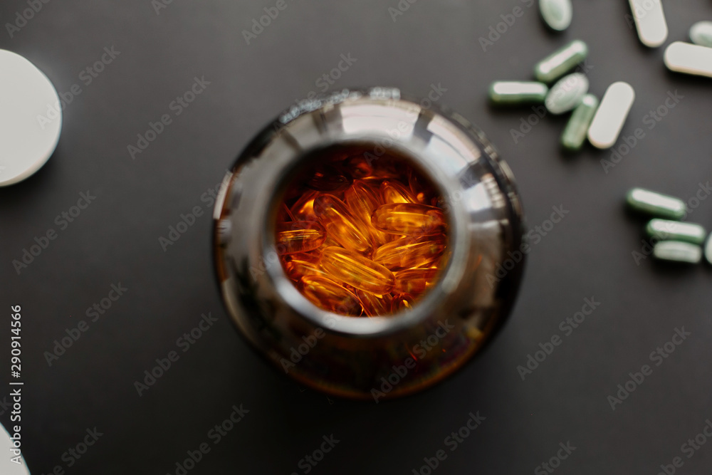 Omega 3 capsules in jar bottle and dietary supplements pills on black dark background. Top view. Health support and treatment. Biologically active additives. Omega 3 capsules in jar bottle and dietary supplements pills on black dark background. Top view. Health support and treatment. Biologically active additives.