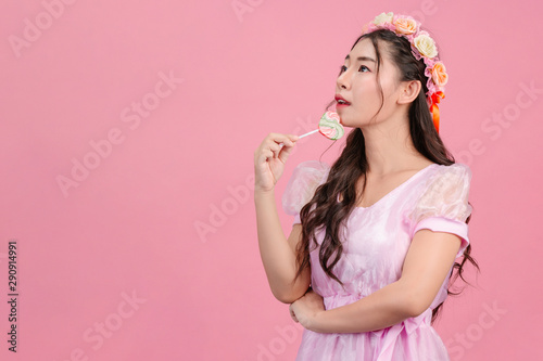 A beautiful woman dressed in a pink princess is playing with her sweet candy on a pink background.