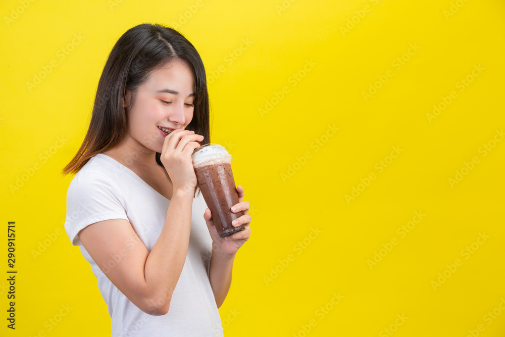 The girl drinks cold water from cocoa from a clear plastic glass on a yellow background. The girl drinks cold water from cocoa from a clear plastic glass on a yellow background.