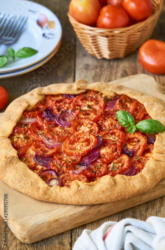 Galette with tomatoes and red onions on a wooden board