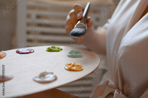 The girl holds art wooden painting palette with different colors and a brush. Painting tools. 