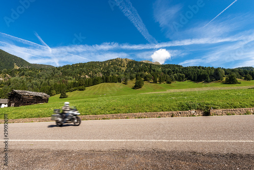 Green meadows and woods in mountain with a biker moving on asphalt road, Viezzena peak. Val di Fiemme, Bellamonte village, Predazzo, Trentino Alto Adige, Italy, Europe photo