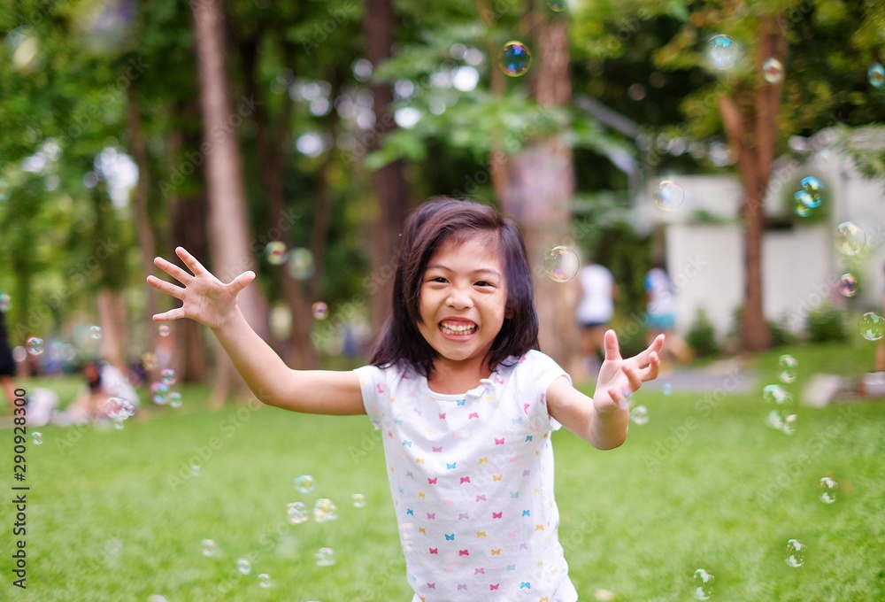 A cute Asian girl playing with bubbles, laughing and smiling.