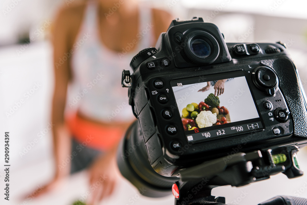 selective focus of digital camera with sportswoman gesturing near vegetables on screen