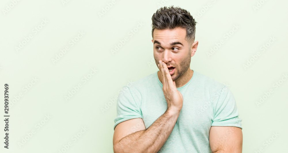 Young handsome man against a green background is saying a secret hot braking news and looking aside Young handsome man against a green background is saying a secret hot braking news and looking aside