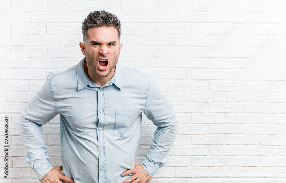 Young handsome man against a bricks wall screaming very angry and aggressive. Young handsome man against a bricks wall screaming very angry and aggressive.