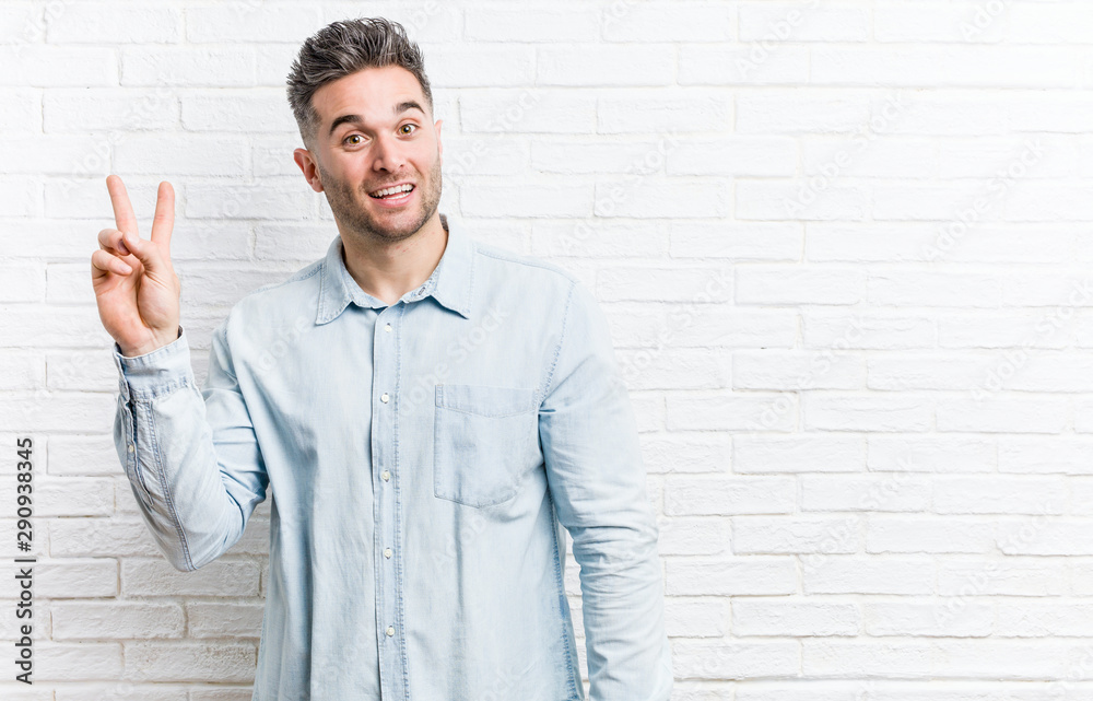Young handsome man against a bricks wall joyful and carefree showing a peace symbol with fingers. Young handsome man against a bricks wall joyful and carefree showing a peace symbol with fingers.
