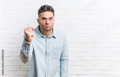 Young handsome man against a bricks wall showing fist to camera, aggressive facial expression.