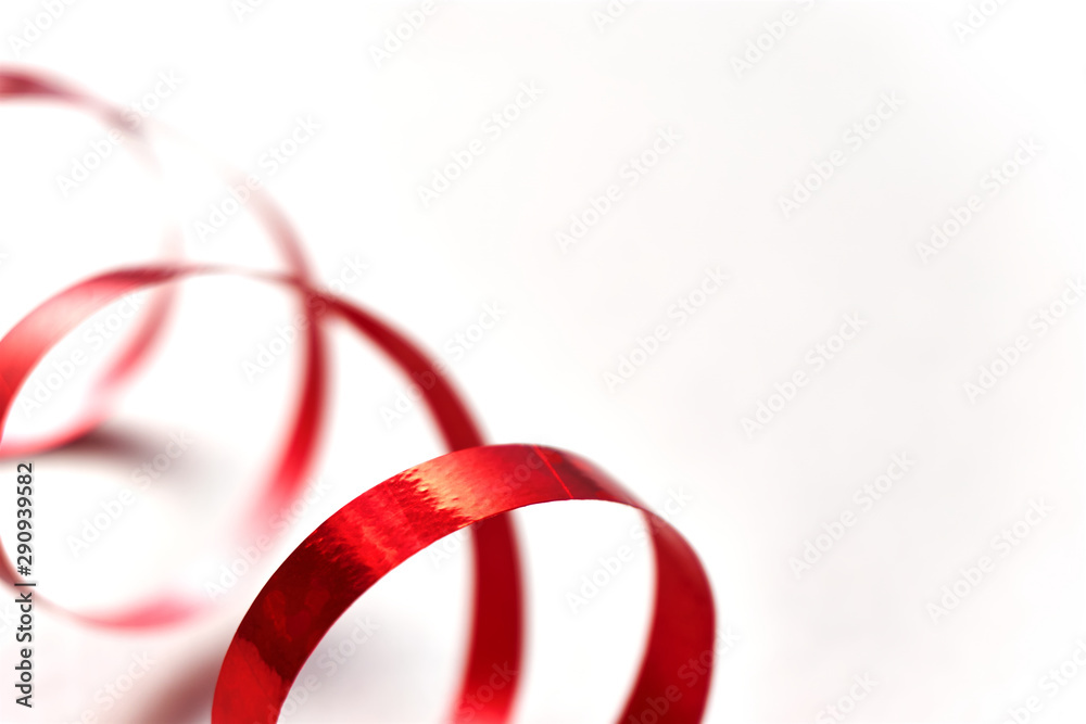 Fototapeta premium Red curly ribbon on white background. Abstract image of serpentine with curls for use as a christmas, anniversary, valentine or celebration background with copy space. 