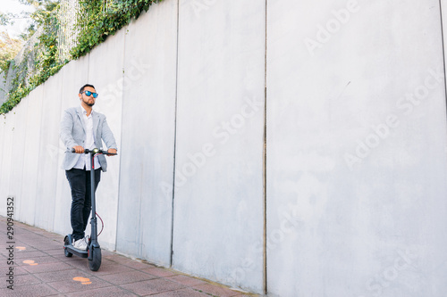 Latin adult man with sunglasses, well dressed and electric scooter on the street with a white blind background © pedro