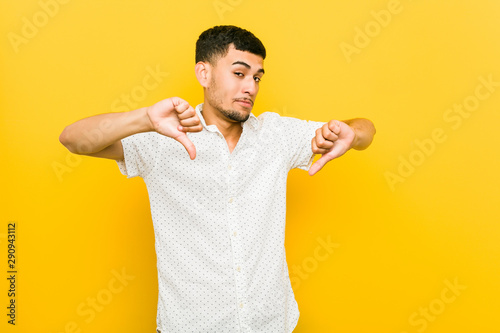 Young hispanic man showing thumb down and expressing dislike.