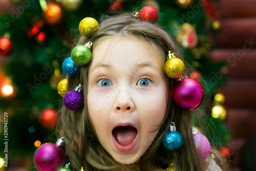 Merry girl on new years eve girl with a garland and Christmas balls in her hair on her head laughing before Christmas