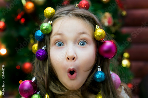 Little girl with garland and Christmas balls in her hair on her head laughing before Christmas