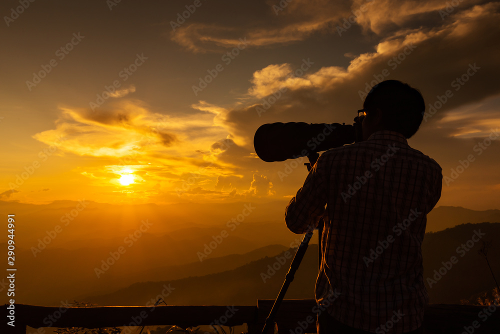 Silhouette of a landscape photographer use super telephoto lens at top of mountains during sunset sky