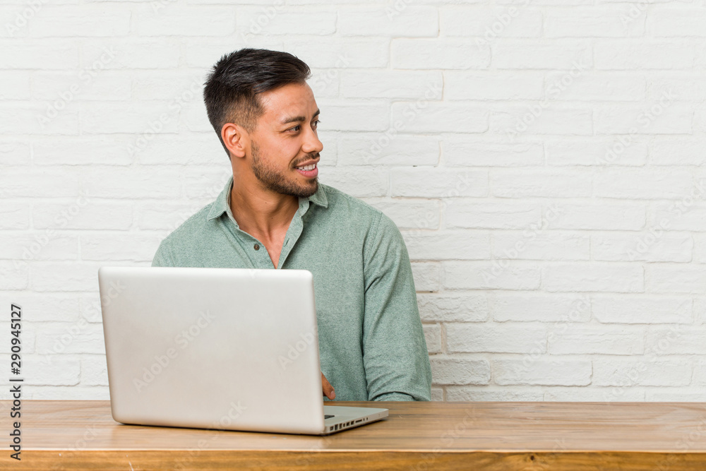 Young filipino man sitting working with his laptop looks aside smiling, cheerful and pleasant. Young filipino man sitting working with his laptop looks aside smiling, cheerful and pleasant.
