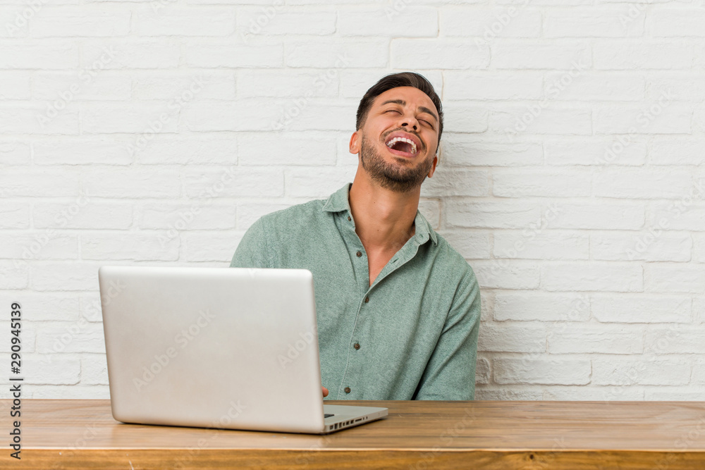 Young filipino man sitting working with his laptop relaxed and happy laughing, neck stretched showing teeth. Young filipino man sitting working with his laptop relaxed and happy laughing, neck stretched showing teeth.