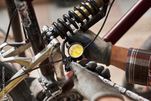 Cropped shot of male bicyclist working in bicycle repair shop, mechanic repairing bike using special tool, wearing protective gloves