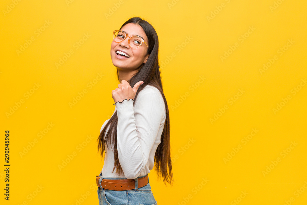 Young pretty arab woman against a yellow background points with thumb finger away, laughing and carefree. Young pretty arab woman against a yellow background points with thumb finger away, laughing and carefree.