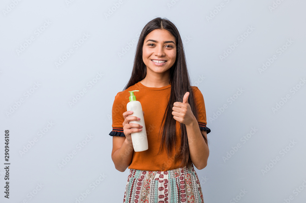 Young arab woman holding a cream bottle smiling and raising thumb up