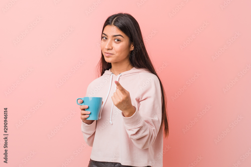 Young arab woman holding a cup pointing with finger at you as if inviting come closer. Young arab woman holding a cup pointing with finger at you as if inviting come closer.