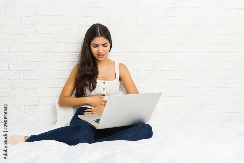 Young arab woman working with her laptop on the bed sick, suffering from stomachache, painful disease concept. Young arab woman working with her laptop on the bed sick, suffering from stomachache, painful disease concept.