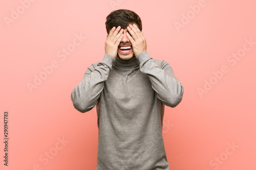 Young smart student man covers eyes with hands, smiles broadly waiting for a surprise.