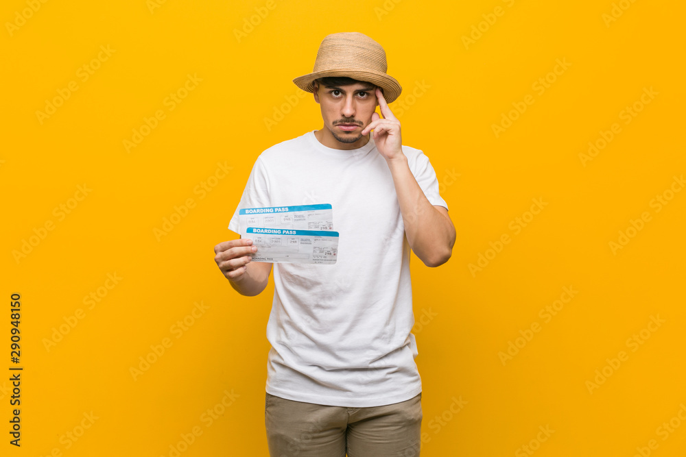 Young hispanic man holding an air tickets pointing his temple with finger, thinking, focused on a task.
