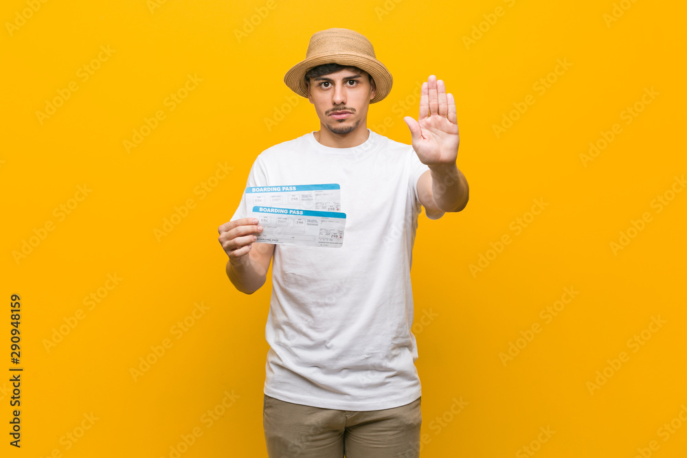 Young hispanic man holding an air tickets standing with outstretched hand showing stop sign, preventing you.