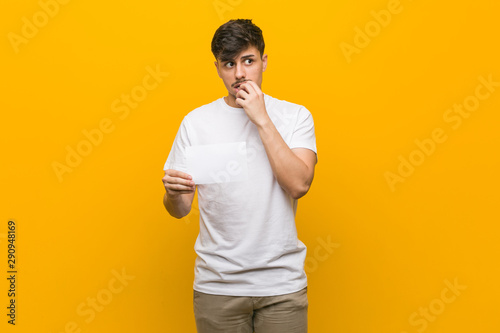 Young hispanic man holding a placard relaxed thinking about something looking at a copy space.