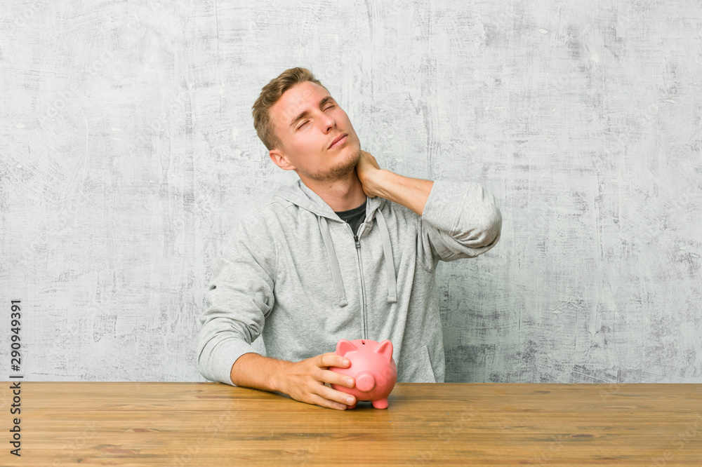 Fototapeta premium Young man saving money with a piggy bank suffering neck pain due to sedentary lifestyle.