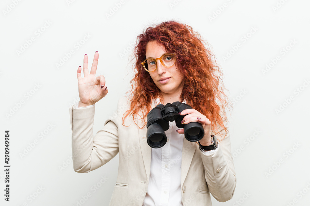 Young caucasian business redhead woman holding a binoculars cheerful and confident showing ok gesture. Young caucasian business redhead woman holding a binoculars cheerful and confident showing ok gesture.