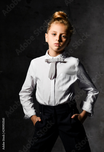 Little female caucasian model posing in school uniform on a gray concrete studio background.
