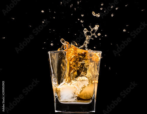 glass of whiskey with ice and a splash and spray from falling on a black background