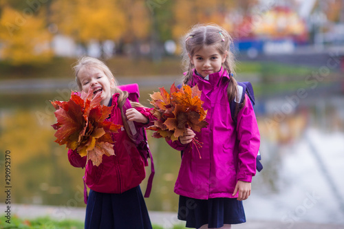 two little smiling girls in school uniform with autumn leaves in park
