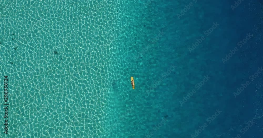 Aerial view of woman paddling on a yellow longboard surfboard in pristine blue ocean water, woman surfing in lagoon