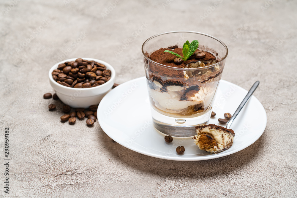 Portion of Classic tiramisu dessert in a glass cup on concrete background Portion of Classic tiramisu dessert in a glass cup on concrete background