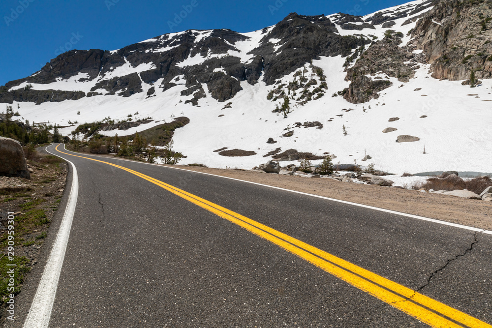 Naklejka premium Low angle view of a road snaking to the horizon in a snow-covered mountain environment