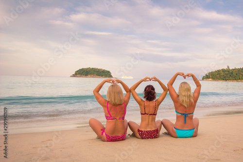 Fototapeta Naklejka Na Ścianę i Meble -  Three girls in swimsuits meet the dawn on the beach. Girls sitting on the sand in the Lotus position. The concept of rest, relaxation yoga. Thailand Phuket, Kata Beach