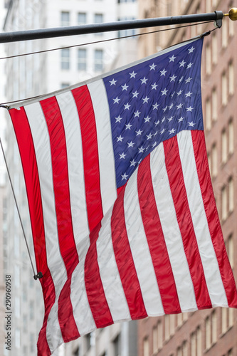 Photography Close up of an american flag waving in the wind, with high-rise buildings in the