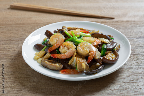 stir fried shiitake mushroom and shrimp with soy sauce in a ceramic dish on wooden table, close up. homemade style food concept.