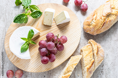 Flat lay overhead composition with fresh organic Camembert cheese with aromatic basil, ripe red grapes and French baguette. Tasty French style lunch. Template  culinary blog social media. photo