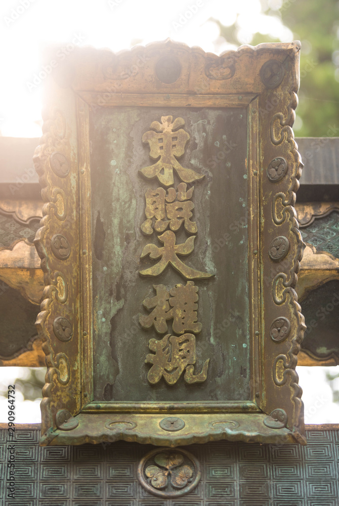 Close up of an ancient bronze japanese inscription flooded in light in a shinto temple
